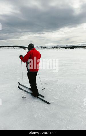 Homme en manteau rouge ski de fond dans le ciel nuageux sur le lac gelé Banque D'Images