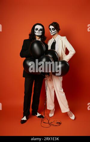 pleine longueur de couple en maquillage de crâne et costumes avec ballons noirs sur rouge, dia de los muertos partie Banque D'Images