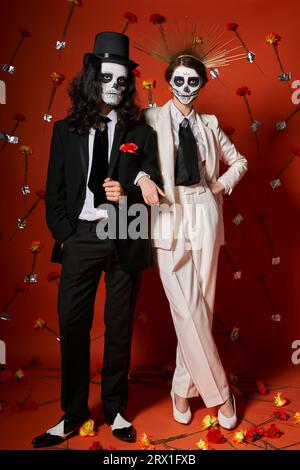 longueur complète de couple élégant festif en dia de los muertos maquillage sur fond rouge avec décor floral Banque D'Images