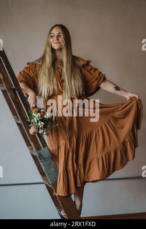 Femme en robe longue sur l'échelle de la bibliothèque Banque D'Images