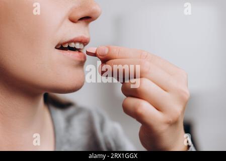 Gros plan de souriante femme caucasienne prenant la pilule ronde, heureuse jeune femme de 25 ans prenant supplément le matin, vitamines quotidiennes pour les cheveux et la peau Banque D'Images