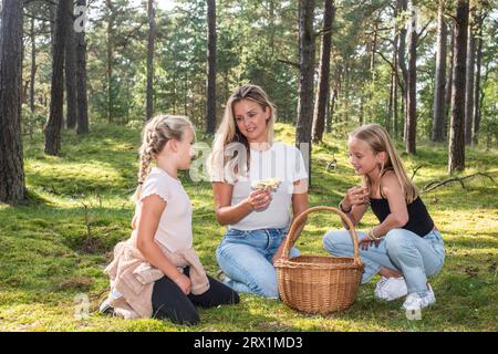 Femme blonde avec deux filles, 7 et 10 ans, à la recherche de champignons dans la forêt à Ystad, Scania, Suède, Scandinavie Banque D'Images