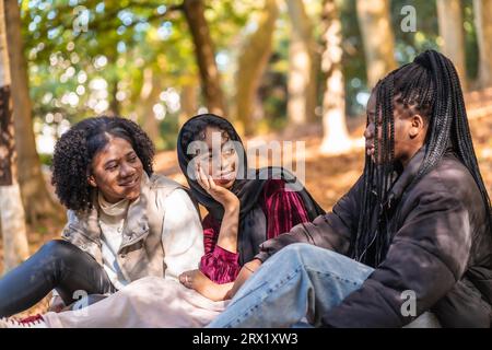 Groupe de trois amis multiculturels assis détendu sur un parc Banque D'Images