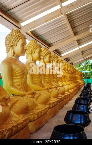 Ancienne rangée de statues de Bouddha d'or avec des bols de moines en métal pour offrir dans le temple thaïlandais Banque D'Images