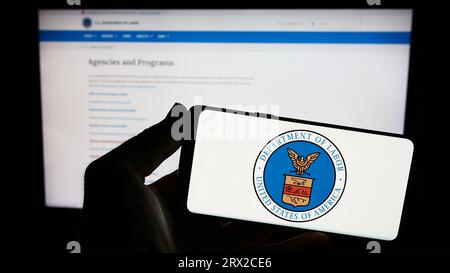 Personne tenant le smartphone avec le sceau du Département du travail des États-Unis (US DOL) sur l'écran en face du site Web. Concentrez-vous sur l'affichage du téléphone. Banque D'Images