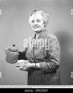 Le café dans les années 1960 Une dame âgée tient une cafetière et une tasse qui semble heureuse. Suède 1955 Kristoffersson Réf BT50-12 Banque D'Images