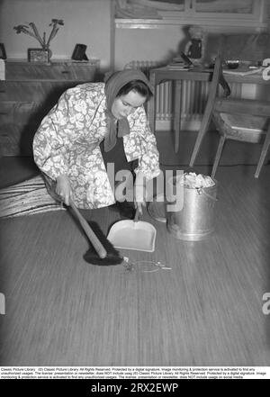 La jeune étudiante d’Uppsala, Eva-Britt Ohlsson, nettoie et balaie le sol de la poussière et de la saleté un jour de février 1940. Pour ce faire, elle s'est habillée d'un manteau de nettoyage et ses cheveux d'une écharpe. Une commode, une table et une chaise sont visibles dans la chambre étudiante de la résidence étudiante à Uppsala. Suède 1940. Kristoffersson ref 54-1 Banque D'Images