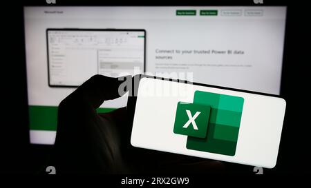 Personne tenant le téléphone mobile avec le logo de l'éditeur de feuille de calcul Microsoft Excel sur l'écran en face de la page Web de l'entreprise. Concentrez-vous sur l'affichage du téléphone. Banque D'Images