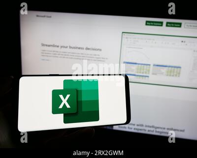 Personne tenant le téléphone portable avec le logo de l'éditeur de feuille de calcul Microsoft Excel sur l'écran en face de la page Web d'affaires. Concentrez-vous sur l'affichage du téléphone. Banque D'Images