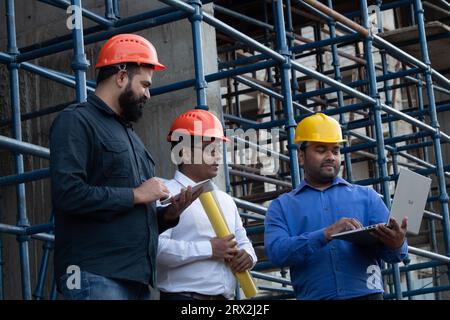 Trois ingénieurs des membres du Conseil de développement de l'industrie de la construction planifient l'utilisation d'un ordinateur portable, d'un plan et d'un bloc-notes sur le site du projet Banque D'Images