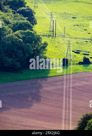 Câbles électriques à haute tension, suspendus aux pylônes en acier, passant vers l'ouest, sur les champs verts et les terres agricoles de l'Angleterre rurale pittoresque, reflec Banque D'Images