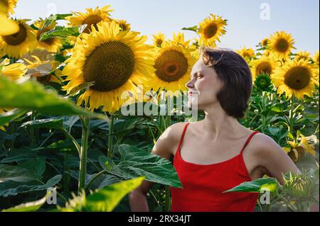 Belle jeune femme avec des tournesols appréciant la nature et riant sur le champ de tournesol d'été. Femme tenant des tournesols. Rayons de soleil, rayons de soleil, rayons de soleil phosphorescents, Banque D'Images