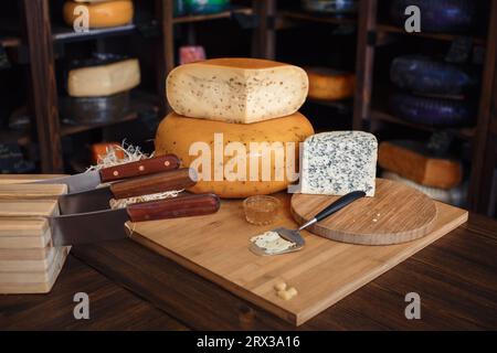 Les têtes de fromage avec des tranches et des couteaux reposent sur une planche de bois avec un intérieur Banque D'Images