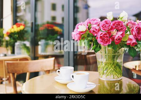 Vase avec des fleurs roses et deux tasses de café dans un café en plein air, concept d'amour et de romance Banque D'Images