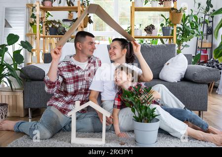 Famille traditionnelle avec enfant apprécient la nouvelle maison, assis sur le canapé et tenant le toit. Hypothèque, assurance et protection, achat et déménagement i Banque D'Images