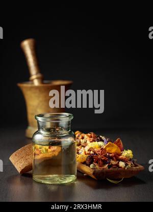 Huile essentielle ou teinture à base de plantes dans une bouteille en verre. Mélange d'herbes médicinales saines séchées et de plantes curatives sur fond noir. Espace de copie. Banque D'Images