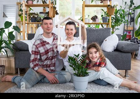 Famille traditionnelle avec enfant apprécient la nouvelle maison, assis sur le canapé et tenant le toit. Hypothèque, assurance et protection, achat et déménagement i Banque D'Images