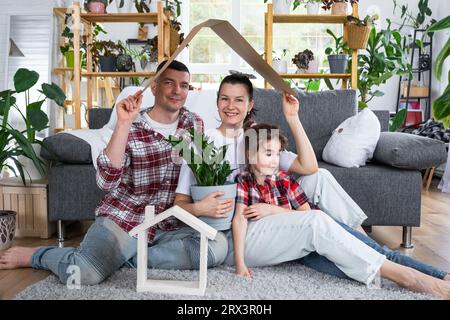 Famille traditionnelle avec enfant apprécient la nouvelle maison, assis sur le canapé et tenant le toit. Hypothèque, assurance et protection, achat et déménagement i Banque D'Images