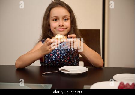 Portrait authentique d'un adorable petit enfant caucasien, une jolie fille d'anniversaire de 6 ans tenant une tartelette française à la crème au citron, sourit mignon Banque D'Images