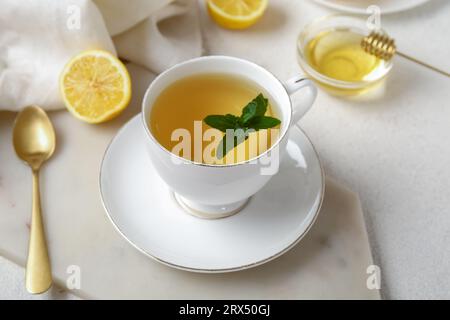 Tasse de thé à la menthe fraîche avec des citrons et du miel sur fond clair grunge Banque D'Images