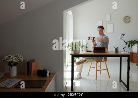 Freelance dans les gros titres assis au bureau dans le bureau à domicile et vérifier la notification sur smartwatch Banque D'Images