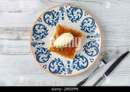 Kunefe avec des pistaches et de la crème glacée sur une assiette en porcelaine sur une table en bois Banque D'Images