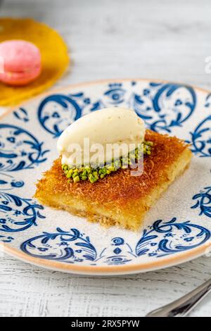 Kunefe avec des pistaches et de la crème glacée sur une assiette en porcelaine sur une table en bois Banque D'Images