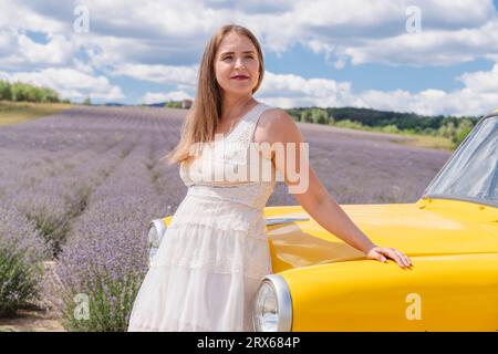 Femme souriante appuyée sur la voiture jaune par le champ de lavande Banque D'Images