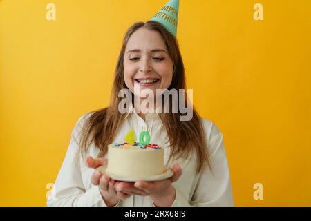 Femme heureuse portant un chapeau de fête tenant le gâteau d'anniversaire Banque D'Images