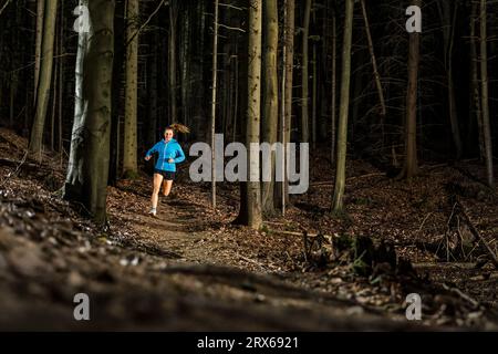Déterminé jeune sportswoman jogging au milieu des arbres dans la forêt Banque D'Images