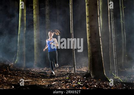 Déterminé jeune sportswoman courir dans la forêt par temps brumeux Banque D'Images
