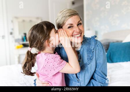 Fille chuchotant dans l'oreille de la mère à la maison Banque D'Images