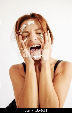 Femme frustrée avec des morceaux de miroir cassés sur le visage criant Banque D'Images