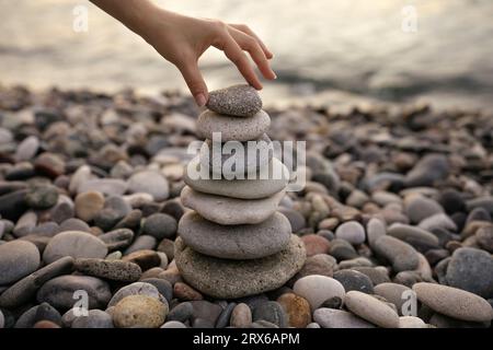 Main de femme empilant des cailloux à la plage Banque D'Images