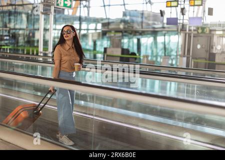 Jeune femme avec valise et tasse à café jetable sur la passerelle mobile Banque D'Images