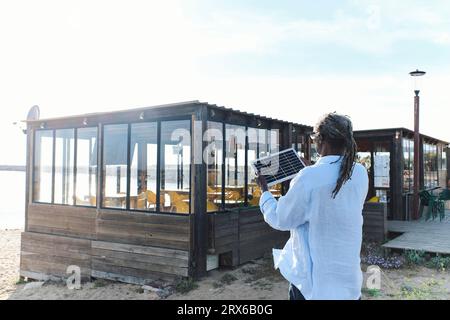 Ingénieur examinant le panneau solaire devant le café à la plage Banque D'Images