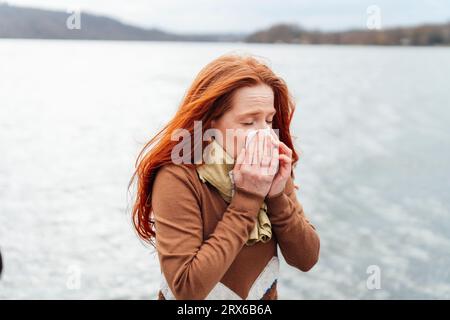 Femme de Redhead soufflant le nez devant le lac Banque D'Images