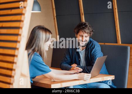 Femme d'affaires souriante discutant sur ordinateur portable avec l'homme d'affaires dans le cubicule de bureau Banque D'Images