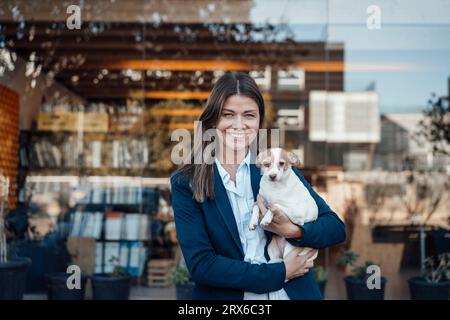 Heureuse femme d'affaires tenant le chien devant le verre Banque D'Images
