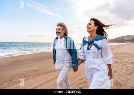 Heureux couple senior se tenant la main marchant à la plage Banque D'Images