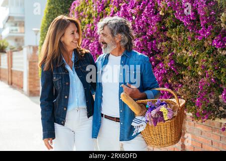 Heureux couple senior avec panier pique-nique debout près du mur de fleurs Banque D'Images