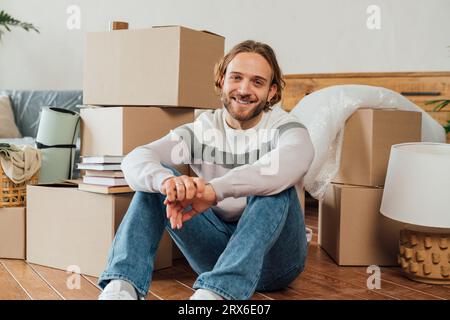 Heureux jeune homme assis avec les mains serrées par des boîtes en carton Banque D'Images