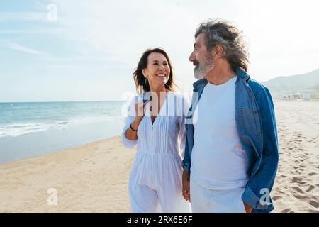 Homme et femme aînés souriants debout à la plage le jour ensoleillé Banque D'Images