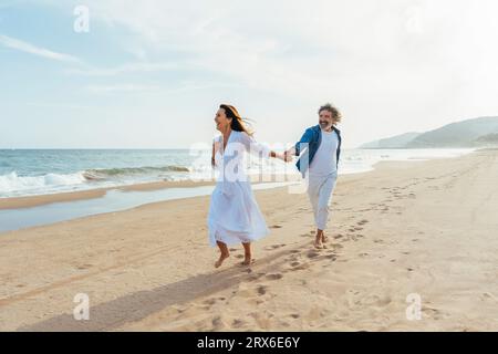 Heureuse femme âgée tenant la main avec l'homme et marchant sur le rivage Banque D'Images