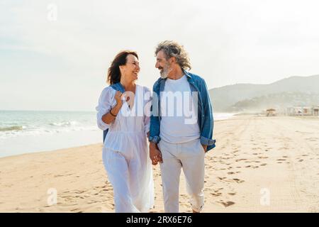 Heureux homme senior et femme marchant à la plage le jour ensoleillé sous le ciel Banque D'Images