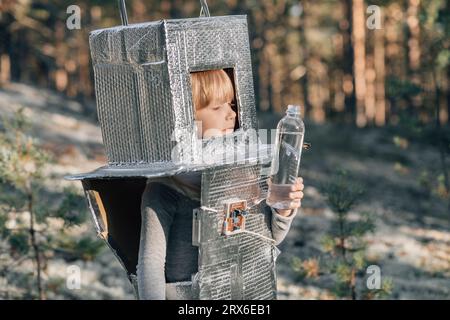 Garçon portant le costume d'astronaute et tenant la bouteille d'eau dans la forêt Banque D'Images