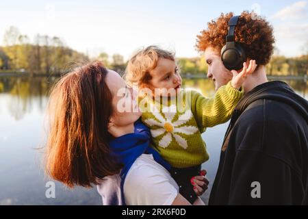 Mère portant sa fille jouant avec les écouteurs de son frère dans le parc Banque D'Images