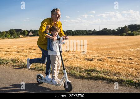 Homme heureux et garçon chevauchant le scooter de poussée sur la route Banque D'Images