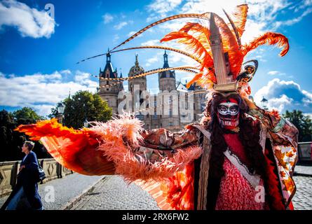 Schwerin, Allemagne. 23 septembre 2023. Porter un costume coloré et un chapeau avec le St. La Tour de Marc, l'un des quelque 300 porteurs de costumes et de masques, se tient devant le château de Schwerin pendant les jours vénitiens dans la capitale de l'État. Un souffle du carnaval vénitien amène les fans de costumes de toute l'Europe autour du château de Schwerin. En plus des visites de la ville, de l'agitation du marché, des concerts et des lectures de livres, des promenades en gondole font également partie du programme. Crédit : Jens Büttner/dpa/Alamy Live News Banque D'Images