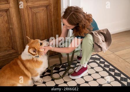 Jeune femme caressant chien assis sur le tapis à la maison Banque D'Images